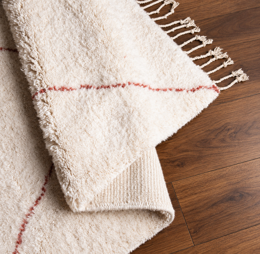Folded detail of handmade Moroccan ivory and terracotta diamond wool rug on warm walnut wood floor