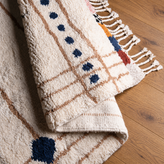 Folded detail of handmade Moroccan cream multicolor abstract wool rug with fringe