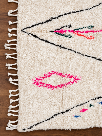 Close detail of handmade Moroccan ivory and pink Berber wool rug with fringe and colorful accents